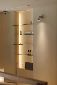 Bathroom with a shelf filled with bottles and a book, featuring a white color scheme and soft warm lighting