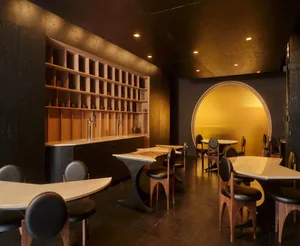 A modern restaurant with a large dining area, bar, and comfortable seating, featuring a variety of tables, chairs, and bottles on display