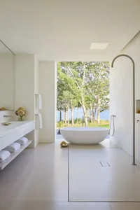 A modern bathroom with a white bathtub, sink, and window, featuring a clean and minimalist design with white tiles and walls, and natural light from the window