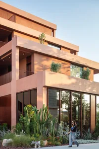 A modern building with a pink and brown color scheme, featuring a large balcony and various windows, with natural light streaming in through the windows
