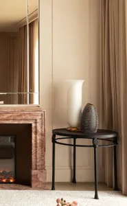 A modern room with a white wall, a brown table, a mirror, and a vase, featuring a clean and minimalist design, well-lit with a calm and serene atmosphere