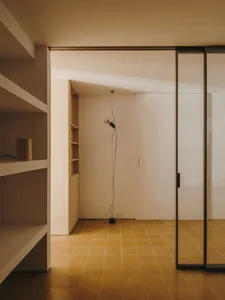 A small, dimly lit room with a yellow floor, white walls, and a doorway and window