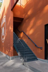 A modern staircase with a brick wall and metal railings, set in a residential area with a red color scheme and natural lighting