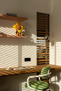 A calm and organized home office with a wooden desk, chair, and shelf, featuring a book and a cup, with natural light from a window