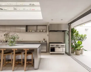 Well-lit modern kitchen with a large island, two dining tables, and various appliances, surrounded by white walls and a silver countertop
