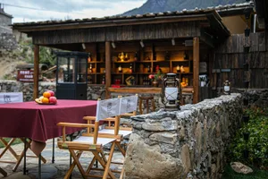 Cozy rustic bar and dining area with a stone wall, wooden table, and chairs, dim lighting creating a warm ambiance
