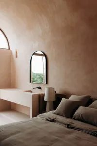 Cozy bedroom with a wooden bed, a wooden bench, and a stone sink, under natural lighting