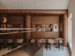Cozy living and dining space with wooden walls and ceiling, featuring a dining table and chairs, books, and a clock on the wall
