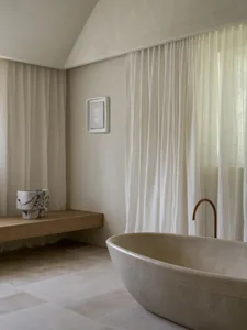 A bathroom with a large white bathtub, a sink, and a bench, surrounded by natural light and a white color scheme