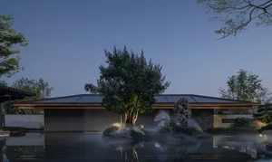 A serene modern house with a pool and a rock garden, surrounded by a large tree, with a blue pool and natural evening lighting