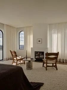 Cozy living room with a fireplace, wooden furniture, and a rug, surrounded by natural light from the windows