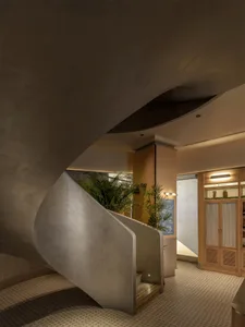 A dimly lit hallway with a spiral staircase and metal railing, featuring a potted plant at the base