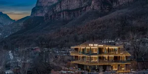 A modern hotel building with a yellow and brown exterior, situated in front of a mountain, with natural light and an inviting atmosphere