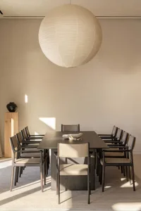 一間充滿自然光線的餐廳，擺放著一張大型木製餐桌和椅子、沙發和一盆植物，桌上擺放著碗和花瓶