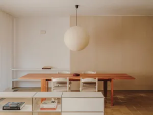 A warm and inviting living room with a wooden dining table, chairs, couch, and bookshelf, lit by natural sunlight