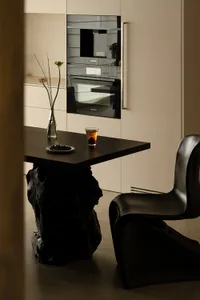 A modern kitchen with a black chair and table, featuring a black oven and microwave, with dim lighting creating a cozy atmosphere