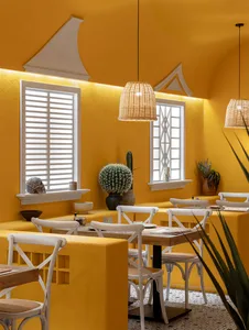 Cozy modern restaurant with a yellow wall, white furniture, and potted plants, warm lighting, and a dining area with tables and chairs