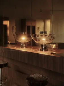 A well-lit bar area with wooden countertops, glass barrier, and decorative vases and wine glasses