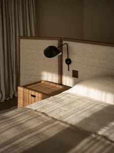 A well-lit bedroom with a bed, nightstand, and lamp, featuring wood and fabric materials in a calm and relaxing environment