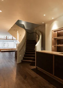 A dimly lit room with a spiral staircase and wooden railing, set against a wooden floor