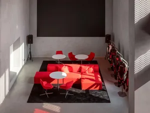 A modern living room with a black wall, red carpet, a large red couch, a dining table, and a few chairs, with red pillows adding warmth and comfort to the space