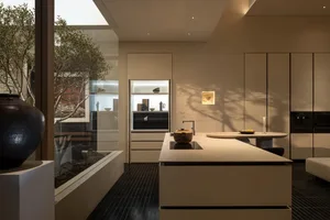Modern kitchen with a white countertop, sink, refrigerator, and oven, adorned with a bowl and vase, in a dimly lit space
