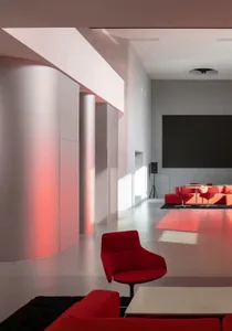 A well-lit lobby with a red chair, ottoman, and dining table, featuring a large screen and comfortable seating