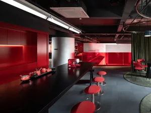 A modern dining space with red walls, a black table, and red chairs, well-lit with natural light from a window