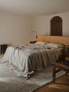 Cozy bedroom with a bed, chair, and lamp, featuring a wooden headboard and a white color scheme, with dim lighting