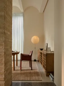 Cozy living room with a brick wall, hardwood floor, a red chair, a table, and a lamp, well-lit and inviting