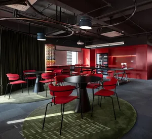A modern dining space with a red and black color scheme, featuring a dining table and chairs, a kitchen area with a refrigerator and sink, and dim lighting creating a warm and intimate ambiance