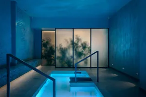 A blue-toned photograph of a swimming pool area with a blue-tiled floor and walls, illuminated by a blue light, creating a unique atmosphere