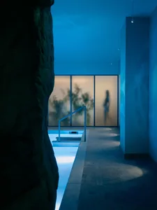 A modern indoor pool area with a blue-lit atmosphere, surrounded by a blue wall and a large rock, creating a relaxing and visually striking environment