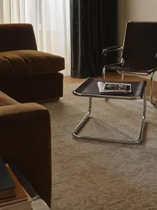 A modern living room with a brown couch, chair, and coffee table, set against a carpeted floor with a magazine on the coffee table