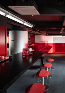 A modern restaurant with a red wall, black counter, and red chairs, featuring apples on the counter and a warm, inviting atmosphere