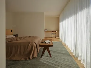 Cozy bedroom with a brown blanket-covered bed, a wooden chair, and a wooden table, set in a well-lit room with a warm atmosphere