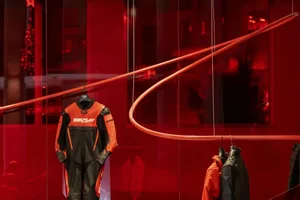 A red room with a circular light and mannequin displaying a black and orange wetsuit, surrounded by other clothing items in a visually appealing retail display