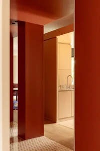 A modern kitchen with a red accent wall, featuring a sink, refrigerator, and dining table, with a focus on functionality and clean lines