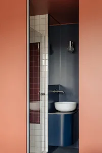 Small modern bathroom with a blue sink, pink wall, and tiled floor, featuring a mirror above the sink and dim lighting