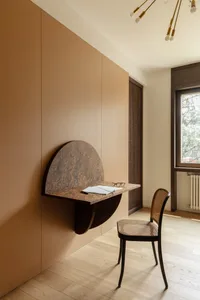 A warm and cozy home office with a wooden floor, a desk, a chair, and a book, lit by natural light from a window