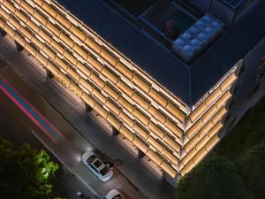夜晚一座大型建築物以人工燈光照亮，對比黑暗的城市天空，前方停有汽車