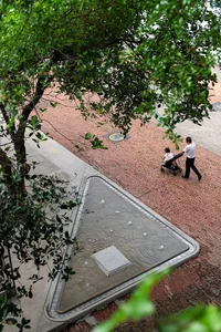 一名男子推著嬰兒車走在都市環境中的磚石人行道上