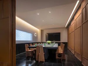 A large dining room with a long wooden table and chairs, set with wine glasses and vases, surrounded by a modern and elegant atmosphere with a large TV on the wall