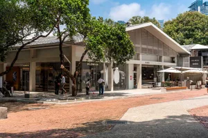 A bustling city storefront with a brick sidewalk, a tree, and a flower shop with a large window and sign, set against a city street background
