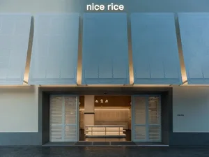 A storefront with a white and blue color scheme, featuring a large window, metal awning, and a sign reading Nice Rice