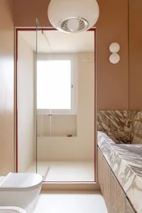 Modern bathroom with a glass shower, a bathtub, and a window, featuring a tiled floor and marble countertop, with natural light coming in through the window