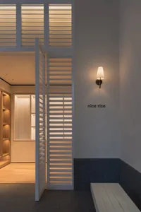 A minimalist kitchen with a white wall, a light fixture, a refrigerator, and a sink, with a focus on functionality and simplicity