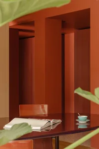 A warm and inviting dining space with a red wall, a wooden table, and a potted plant, set with a cup, a bowl, and a spoon