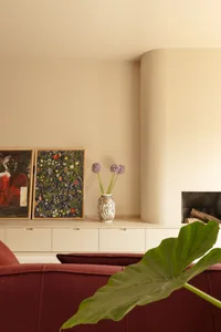 A modern living room with a red couch, white walls, and a fireplace with a vase of flowers on the mantel, two framed pictures on the wall, and a clean, simple aesthetic