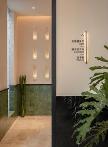 A well-lit bathroom with a green tiled floor, a toilet, a sink, and two potted plants, creating a bright and inviting atmosphere